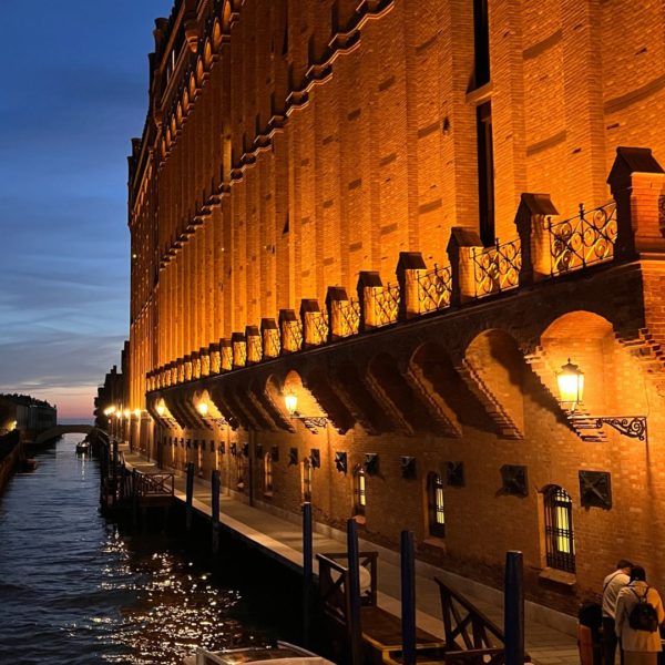 Hotel by night with a boat parked in front of its private pier. A beautiful frontage with red bricks is enlighten.