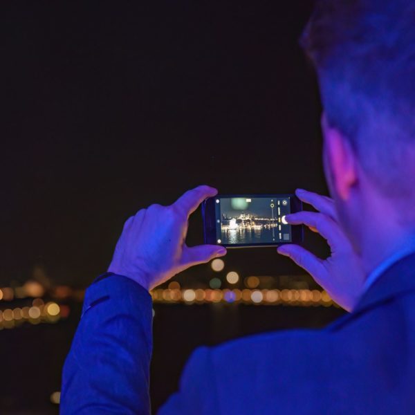 Guest taking a picture with his smartphone of the Venice skyline at night from the rooftop