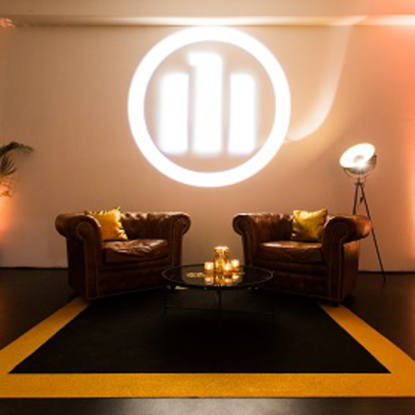 Dark chesterfields with black and gold carpet customer logo projected on the wall to serve as a welcome area