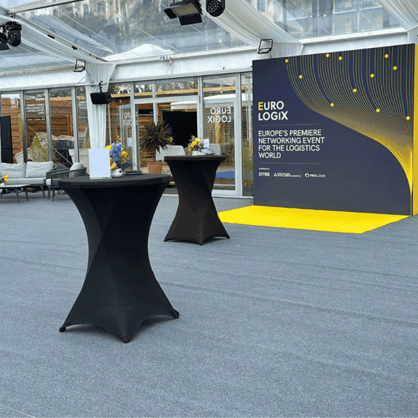 Set-up picture of MIPIM lunch networking event: printed photocall with yellow carpet under a tent on the beach in Cannes with high tables and matching yellow flower compositions