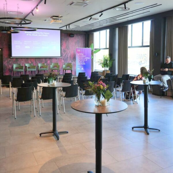 venue set up with theatre format facing the stage and the projection screen as well as some high tables and high stools in the back