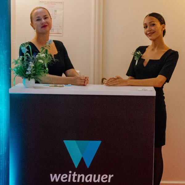 COUPLE OF HOTESSES AT THE BRANDED WLECOME DESK READY TO TAKE THE GUESTS COATS AND LUGGAGES IN THE CLOAKROOM